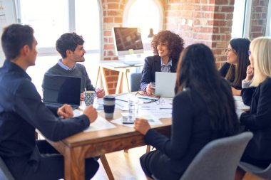 Bir grup iş adamı mutlu ve kendinden emin gülümsüyor. Yüzünde gülümsemeyle çalışmak, dizüstü bilgisayar kullanmak ve ofiste konuşmak.