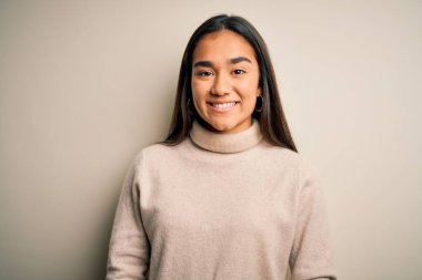 Genç, güzel Asyalı bir kadın beyaz arka plan üzerine balıkçı yaka kazak giyiyor ve yüzünde mutlu ve havalı bir gülümseme var. Şanslı kişi..