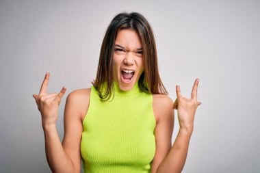 Genç, güzel esmer kız izole edilmiş beyaz arka plan üzerine gündelik tişört giyip çılgın bir ifadeyle elleri havada rock sembolü yaparak bağırıyor. Müzik yıldızı. Ağır konsept.