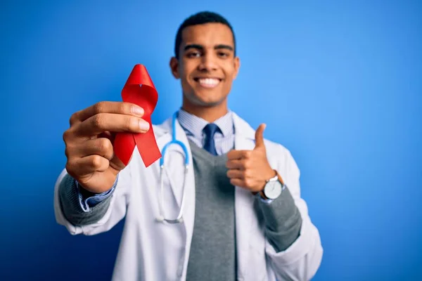 年轻英俊的非洲医生 手持红色艾滋病毒带符号的美国医生 喜形于色 笑容满面 做手势 用手指竖起大拇指 标志出色 — 图库照片