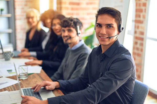 Group of call center workers working together with smile on face using headset. Young handsome man smiling at the office.