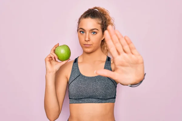 年轻美丽的金发女运动员 蓝眼睛 健康的绿色苹果果实 张开双手 严肃而自信地做着止步手势 做着防守动作 — 图库照片