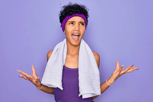 紫色の背景にタオルを着てスポーツをしている美しいアフリカ系アメリカ人のスポーティな女性は 狂気と怒りの叫びと積極的な表現と腕を上げて叫んでいます 欲求不満の概念 — ストック写真