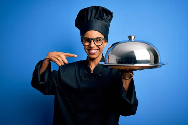 年轻的非洲女厨师 身穿制服 手持圆顶餐盘 手指手画脚 非常高兴 — 图库照片