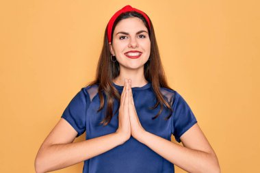 Sarı arka planda kırmızı dudaklar takan genç, güzel esmer kadın elleriyle dua ederek af diliyor kendinden emin bir şekilde gülümseyerek..