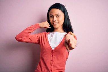 İzole edilmiş pembe arka planda rahat süveter giyen genç, güzel Çinli bir kadın gülümseyip telefon jesti hakkında konuşuyor ve seni işaret ediyor. Ara beni..