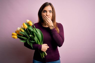 Sarı lalelerden oluşan romantik buketi pembe arka planda tutan genç sarışın kadın yanlışlıkla ağızlarını kapatarak şok geçirdi. Gizli konsept.