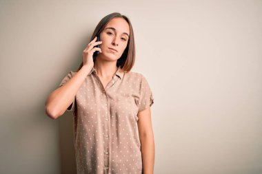 Genç ve güzel bir kadın beyaz arka planda akıllı telefondan konuşuyor. Uykulu ve yorgun görünüyor. Yorgun ve akşamdan kalma, tembel bakışlar..