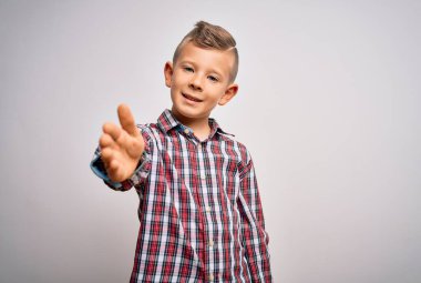 Mavi gözlü, zarif gömlekli, izole edilmiş arka planda duran küçük beyaz bir çocuk dostça bir selamlaşma ve selamlama olarak el sıkışmayı sunuyor. Başarılı bir iş..