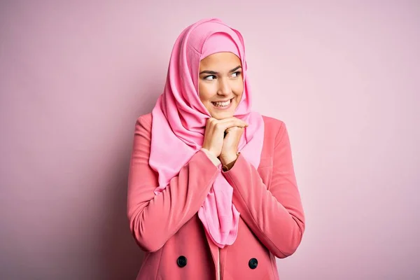 年轻美丽的女孩 戴着穆斯林头巾 站在孤立的粉色背景上 紧张地笑着 双手放在下巴上 朝侧面看去 兴奋极了 — 图库照片