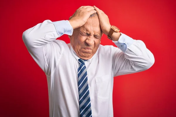 Senior handsome businessman wearing elegant tie standing over isolated red background suffering from headache desperate and stressed because pain and migraine. Hands on head.