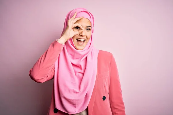 若いです美しいです女の子身に着けていますムスリムヒジャーブ立っています上の隔離されたピンクの背景行いますOkジェスチャーとともに手笑顔 目を通して指で幸せな顔 — ストック写真