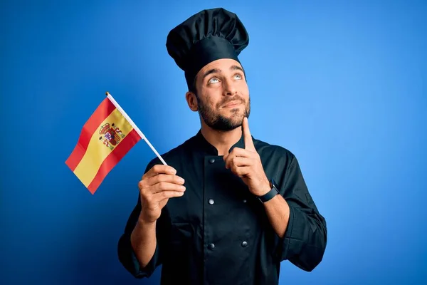 Mladý Pohledný Kuchař Plnovousem Uniformě Držící Španělskou Vlajku Vážný Obličej — Stock fotografie