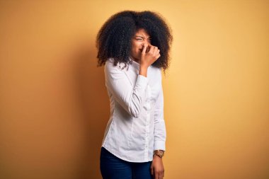 Afro saçlı, genç ve güzel Afro-Amerikan zarif bir kadın sarı arka planda dikilmiş pis ve iğrenç bir koku alıyor, nefesini burnu üzerinde tutuyor. Kötü kokuyor.