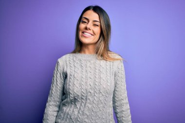 Genç, güzel bir kadın, sıradan bir süveter giyer, mor arka planda durur, kameraya seksi bir ifadeyle bakar, neşeli ve mutlu bir yüzle bakar..