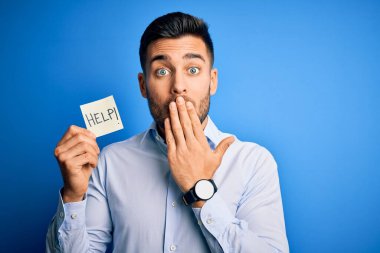 Çok çalışan genç iş adamı mavi arka planda kağıt tutarken yardım istiyor. Ağzını kapayarak hata yaptığı için utancından, korkusunun dışavurumundan, sessizlikten korktuğundan, gizli bir kavramdan bahsediyor.