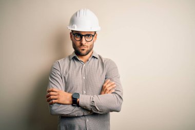 Genç mimar, izole edilmiş arka plan şüphecisi ve gergin kolları çaprazlanmış yüz ifadesini tasvip etmeyen miğfer takıyor. Negatif kişi.
