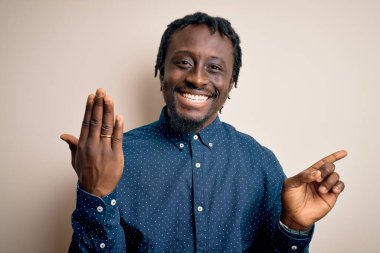 Genç Afrikalı Amerikalı adam beyaz arka planda altın evlilik yüzüğü gösteriyor. Çok mutlu bir şekilde elini ve parmağını kenarı işaret ediyor.