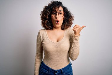 Genç, kıvırcık, kıvırcık bir kadın beyaz arka planda günlük tişört ve gözlük takıyor..