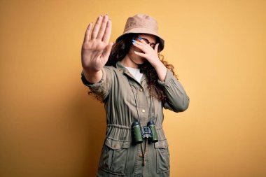 Genç ve güzel bir turist kadın tatilde. Kaşif şapkası ve dürbün takıyor. Gözleri ellerle kaplıyor. Utanç verici ve olumsuz bir kavram..