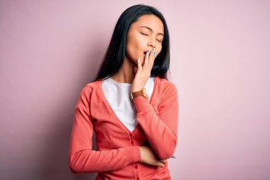 İzole edilmiş pembe arka plan üzerine gündelik kazak giyen genç, güzel Çinli kadın ağzıyla esnemekten sıkılmış. Huzursuz ve uykulu..