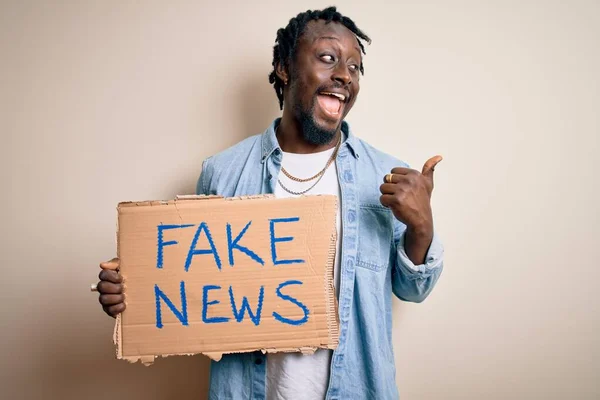 若いですアフリカ系アメリカ人男性保持バナーで偽のニュースメッセージ上の白い背景を指していると幸せな顔笑顔で親指で側まで示す — ストック写真