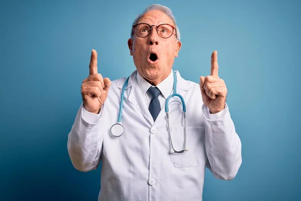 Starszy Siwy Lekarz Noszący Stetoskop Płaszcz Medyczny Niebieskim Tle Zdumiony — Zdjęcie stockowe