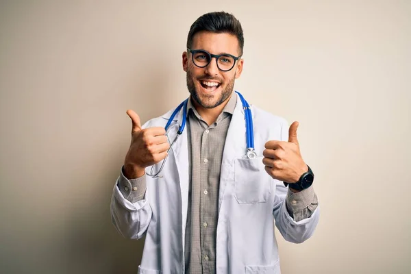 医療用白衣 聴診器を身に着けている若い医師は 手で積極的なジェスチャーを行う孤立した背景の成功サイン上で 親指を笑顔と幸せ 陽気な表情と勝者のジェスチャー — ストック写真