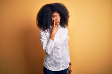 Young beautiful african american elegant woman with afro hair standing over yellow background Pointing to the eye watching you gesture, suspicious expression clipart