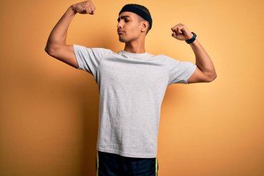 Sarı arka planda spor giyimli yakışıklı Afro-Amerikan sporcu gururla gülümseyen kol kaslarını gösteriyor. Fitness konsepti.