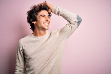 İzole edilmiş pembe arka plan üzerinde duran genç yakışıklı bir adam. Kendine güvenen, el hareketleriyle saçlara dokunan, çekici ve modaya uygun poz veren.