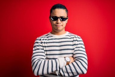 İzole edilmiş kırmızı arka planda güneş gözlüğü takan Brezilyalı genç bir adam. Şüpheli ve gergin. Yüzünde çapraz kollarla onaylamayan bir ifade var. Negatif kişi.