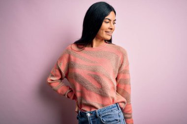 Moda kıyafetleri giyen genç ve güzel bir kadın. Manken, sokak tarzı giyiniyor. Pembe arka planda dikiliyor.