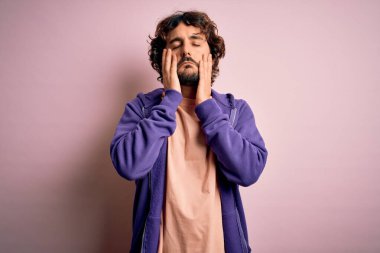 Genç, yakışıklı, sakallı, pembe arka planda rahat bir kazak giyen, yüzü, depresyonu ve üzüntüyü örten, sorun yüzünden sinirli ve sinirli bir adam.