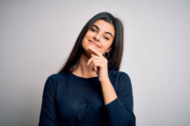 Genç, güzel, esmer bir kadın beyaz arka plan üzerinde sıradan bir süveter giyiyor. Kameraya kendinden emin bir şekilde bakıyor. Kollarını kavuşturup, elini çenesine kaldırmış gülümsüyor. Olumlu düşünüyorum..