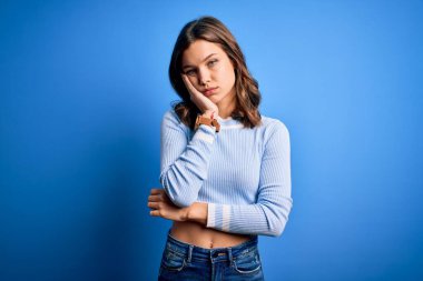 Mavi izole edilmiş arka plan üzerinde duran sıradan bir kazak giyen genç ve güzel sarışın kız kollarını kavuşturarak depresyondan sıkılmış ve yorgun görünüyor..