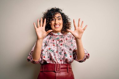 Genç, kıvırcık Arap bir kadın, çiçekli tişört giyiyor. İzole edilmiş beyaz arka planda duruyor. Korkudan ve korkudan ödü patlıyor. Panik konsepti.