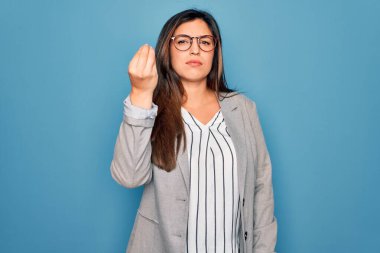 Genç İspanyol iş kadını mavi soyutlanmış arka planda duran gözlük takıyor. İtalyan jestleri yapıyor. El ve parmakları kendinden emin.