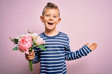 Küçük beyaz çocuk pembe arka planda romantik ve şirin bir buket çiçek tutuyor çok mutlu ve heyecanlı, kazanan yüz ifadesi zaferi büyük bir gülümsemeyle kutluyor ve ellerini kaldırıyor.