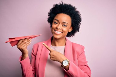 Pembe kâğıt uçak tutan kıvırcık saçlı, genç Afro-Amerikan kadın elini ve parmağını göstererek çok mutluydu.