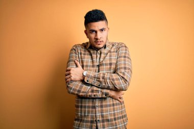 Sarı arka plan üzerinde duran sıradan tişörtlü genç yakışıklı adam kış soğuğu için titriyor ve donuyor. Yüzünde üzgün ve şok ifadesi var.