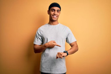 Sarı arka plan üzerine spor giyerek spor yapan yakışıklı Afro-Amerikan sporcusu. Saati, sabırsızlığı ve gecikmeyi izlemek için acele ediyor.