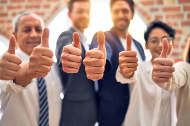 Bir grup iş adamı mutlu gülümsüyor. Ofiste baş parmaklarınla dikiliyorsun.