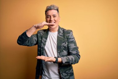 Sarı izole edilmiş arka plan üzerinde duran, büyük ve büyük boyut işareti ve ölçü sembolü gösteren genç, yakışıklı, modern bir adam. Kameraya bakıp gülümsüyor. Ölçüm konsepti.