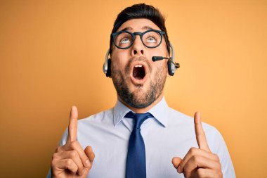 Çağrı merkezinden gelen müşteri hizmetleri kulaklığı takan genç bir işletmeci şaşkın ve şaşırmış bir şekilde yukarı bakıyor ve parmaklarını ve kollarını kaldırıyor..