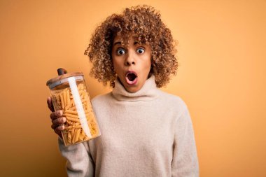 Genç Afro-Amerikan kıvırcık kadın elinde İtalyan makarnası dolu kavanoz tutuyordu. Şok olmuş, şaşırmış ve korku ifadesinden korkmuştu.
