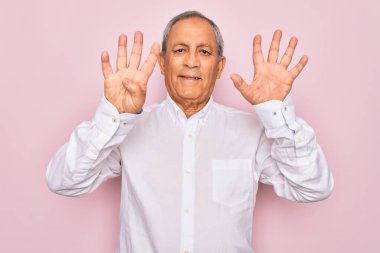 Üst düzey yakışıklı, gri saçlı, zarif tişörtlü, soyutlanmış pembe arka planda, dokuz numarayı işaret eden, kendinden emin ve mutlu gülümseyen bir adam..