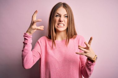 Genç, güzel, kızıl saçlı bir kadın pembe arka plan üzerine günlük süveter giyiyor öfkeden çıldırmış bağırıyor, elleri boğazını sıkmaya çalışıyor, deli gibi bağırıyor.