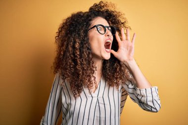 Kıvırcık saçlı, piercingli, çizgili tişörtlü, gözlüklü, bağıran ve ağızdan ağıza bağıran güzel bir kadın. İletişim konsepti.