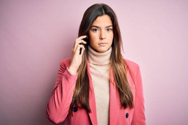 Genç ve güzel bir kız, akıllı telefondan beyaz arka planda konuşuyor. Akıllı bir yüz ifadesiyle ciddi ciddi düşünüyor.